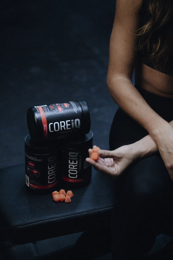 CoreIQ Creatine Gummies jars stacked on a bench, gummies in hand