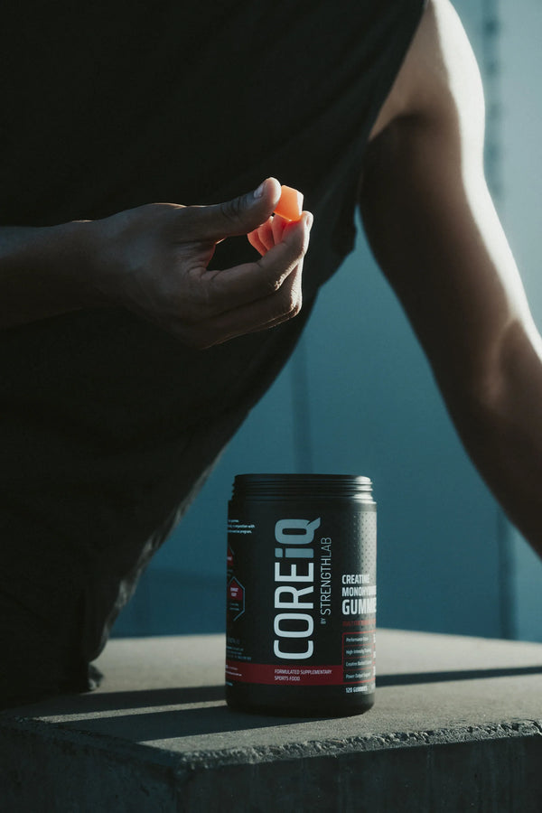 CoreIQ Creatine Gummies jar on a ledge, a gummy in hand