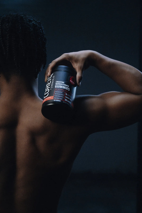 CoreIQ Creatine Gummies jar held on the shoulder in the gym